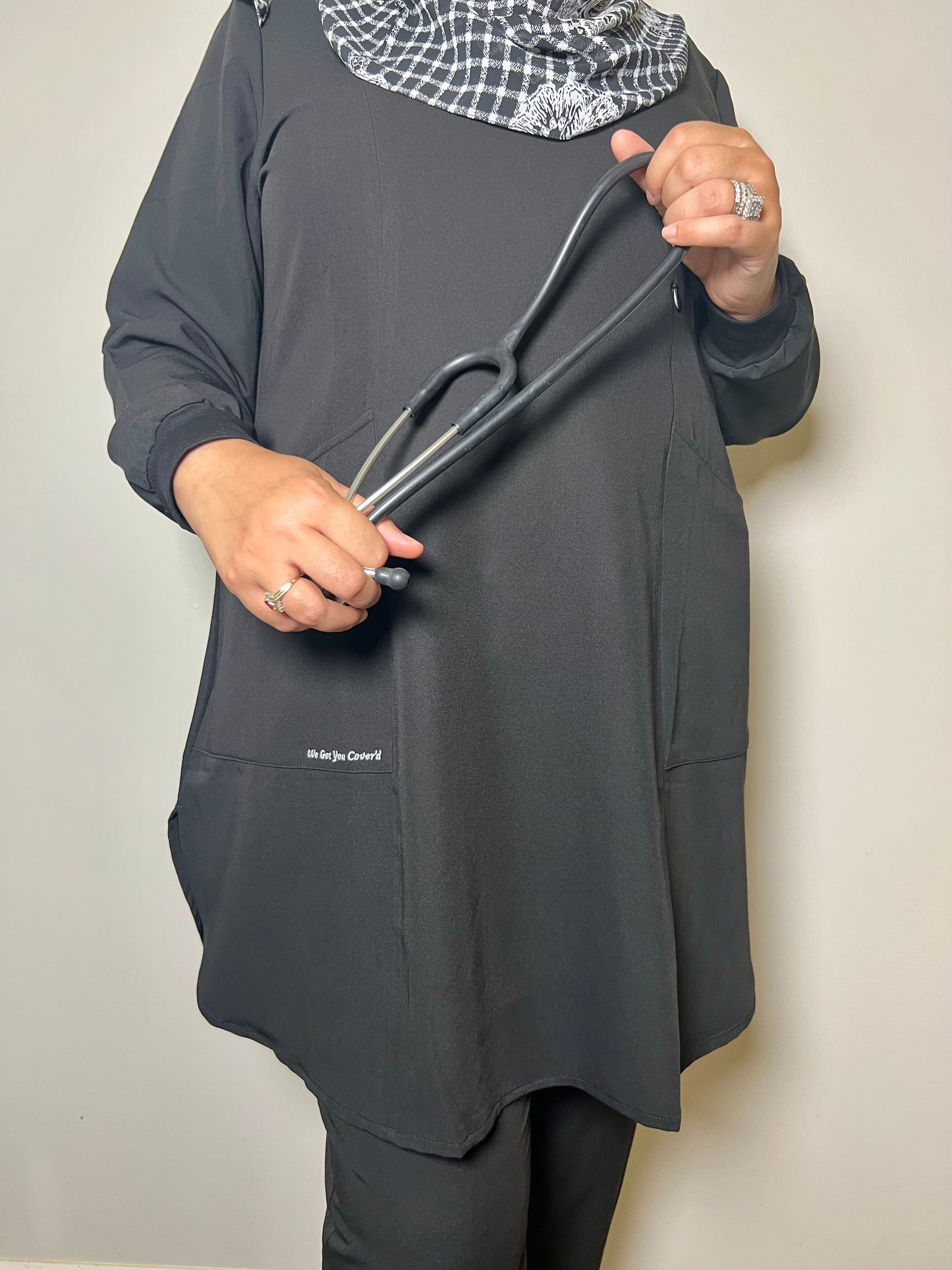 


Woman wearing a black long-sleeve scrub top holding a stethoscope against a plain background